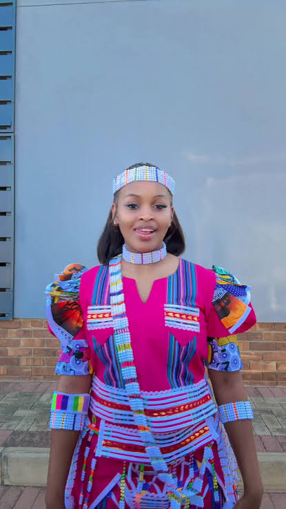 Woman in a vivid pink and multicoloured dress with beaded headband, necklace and cuffs