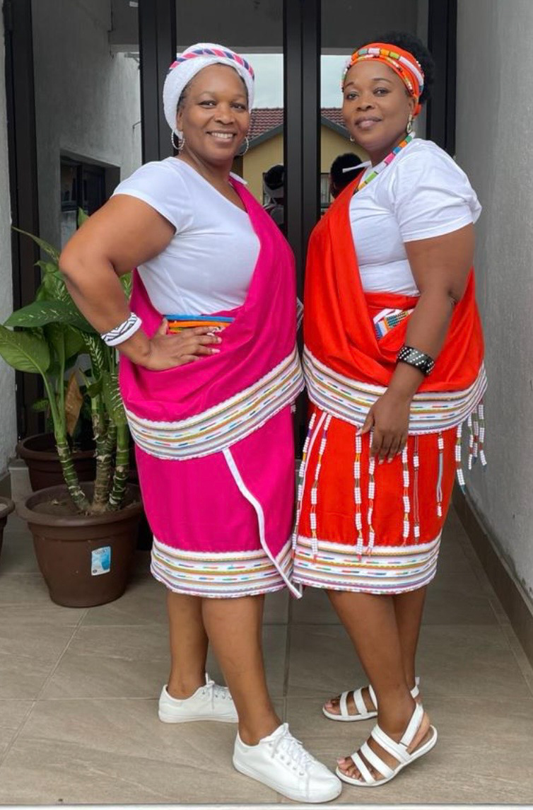 Two women wearing vivid pink and orange wraps edged with multicolored bands