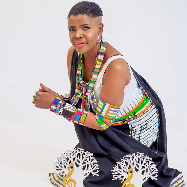 Woman wearing black draped attire with layered colourful beadwork against a white backdrop
