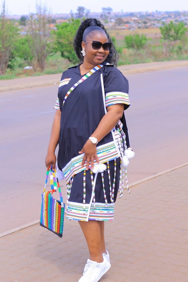 Woman in contemporary black attire with multicoloured trim and a beaded bag