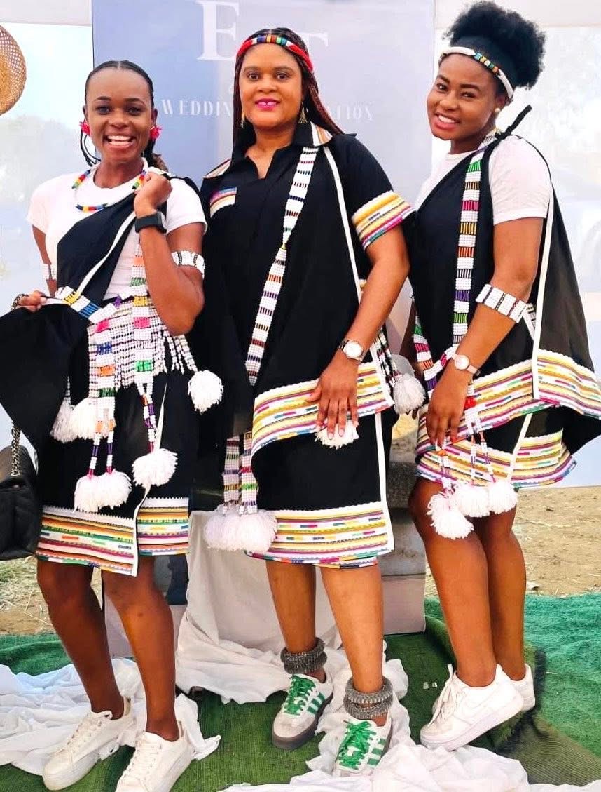 Three women wearing black attire with multicoloured trim and beaded accessories