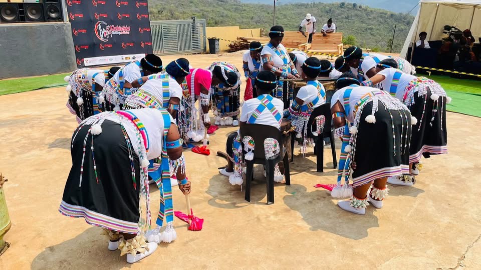 Performers in white and blue attire gathering around seated participants