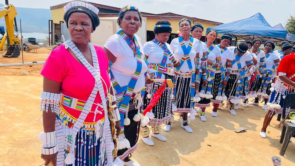 A line of women in white, pink and blue attire with beaded adornments