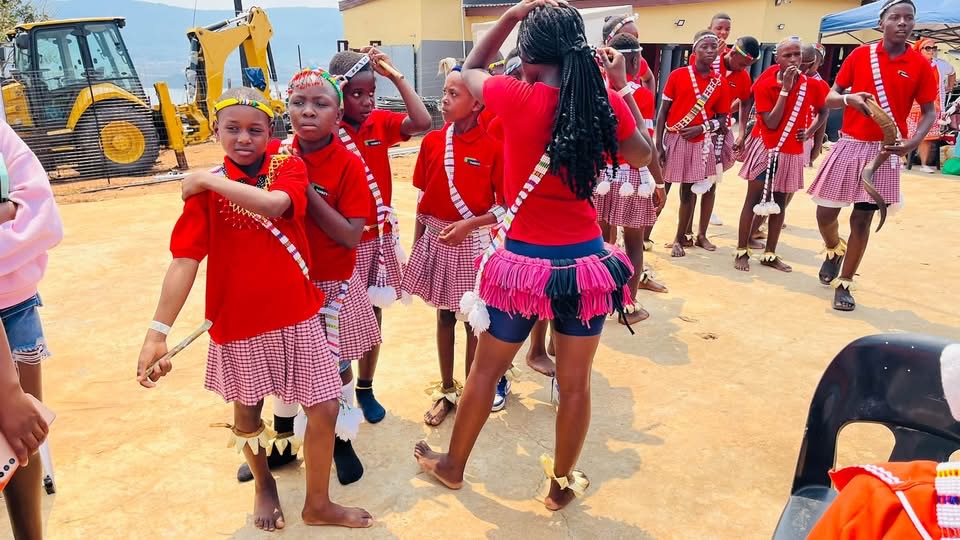 Young performers in red shirts and patterned skirts with beaded sashes