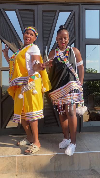 Two women wearing yellow and black attire with multicoloured trim and beadwork